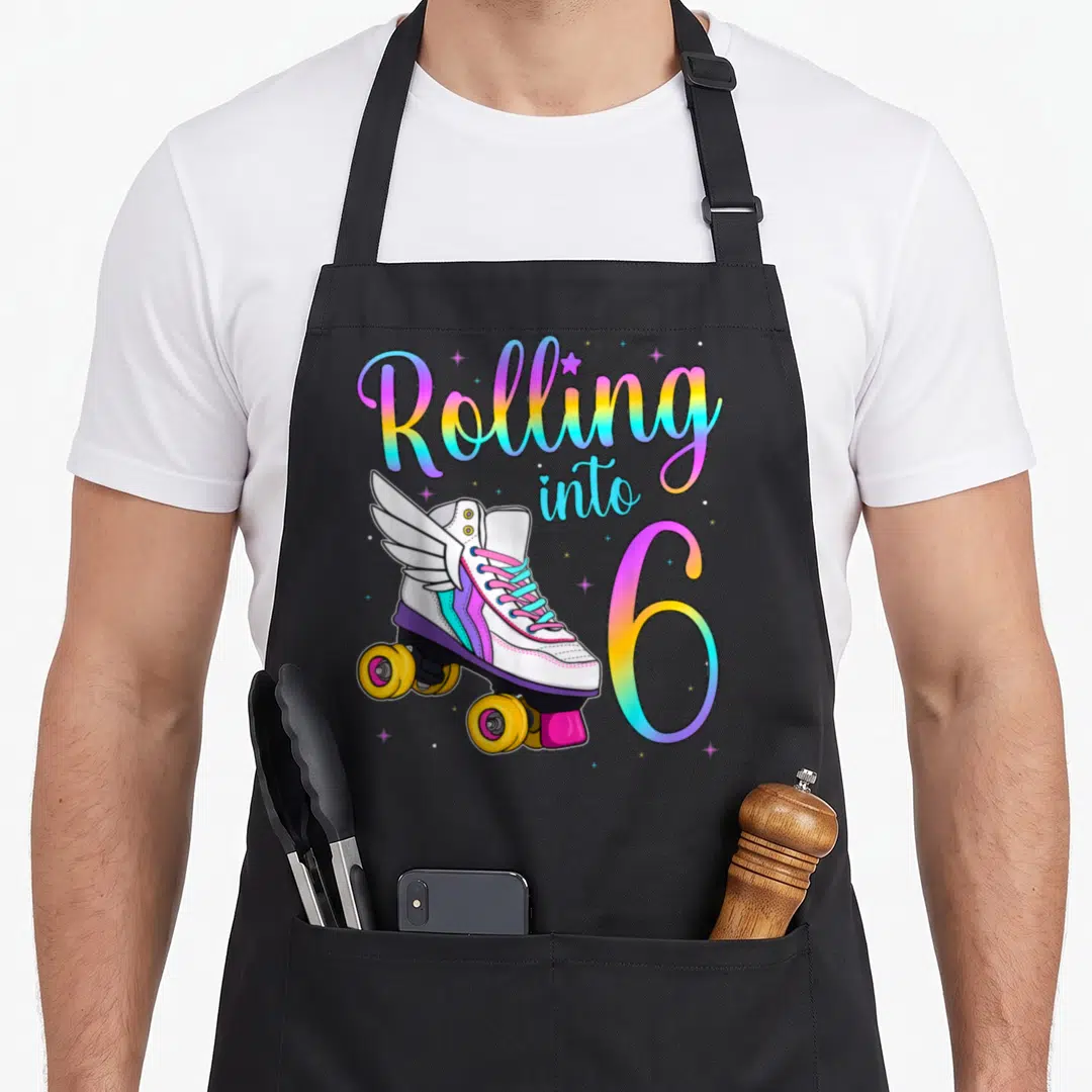 Vintage rolling turning apron - Winged roller skate with rainbow Rolling into 6 text and scattered stars — shown on a black cotton canvas apron against a white background