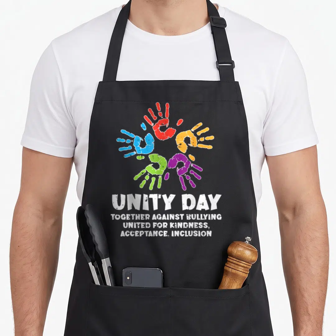 Together unity day apron - Five colorful handprints in a circle above white text reading Unity Day Together Against — shown on a black cotton canvas apron against a white background