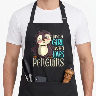 Vintage animal penguin aprons - Cartoon penguin with text just a GIRL WHO loves penguins in purple beige blue white — shown on a black cotton canvas apron against a white background