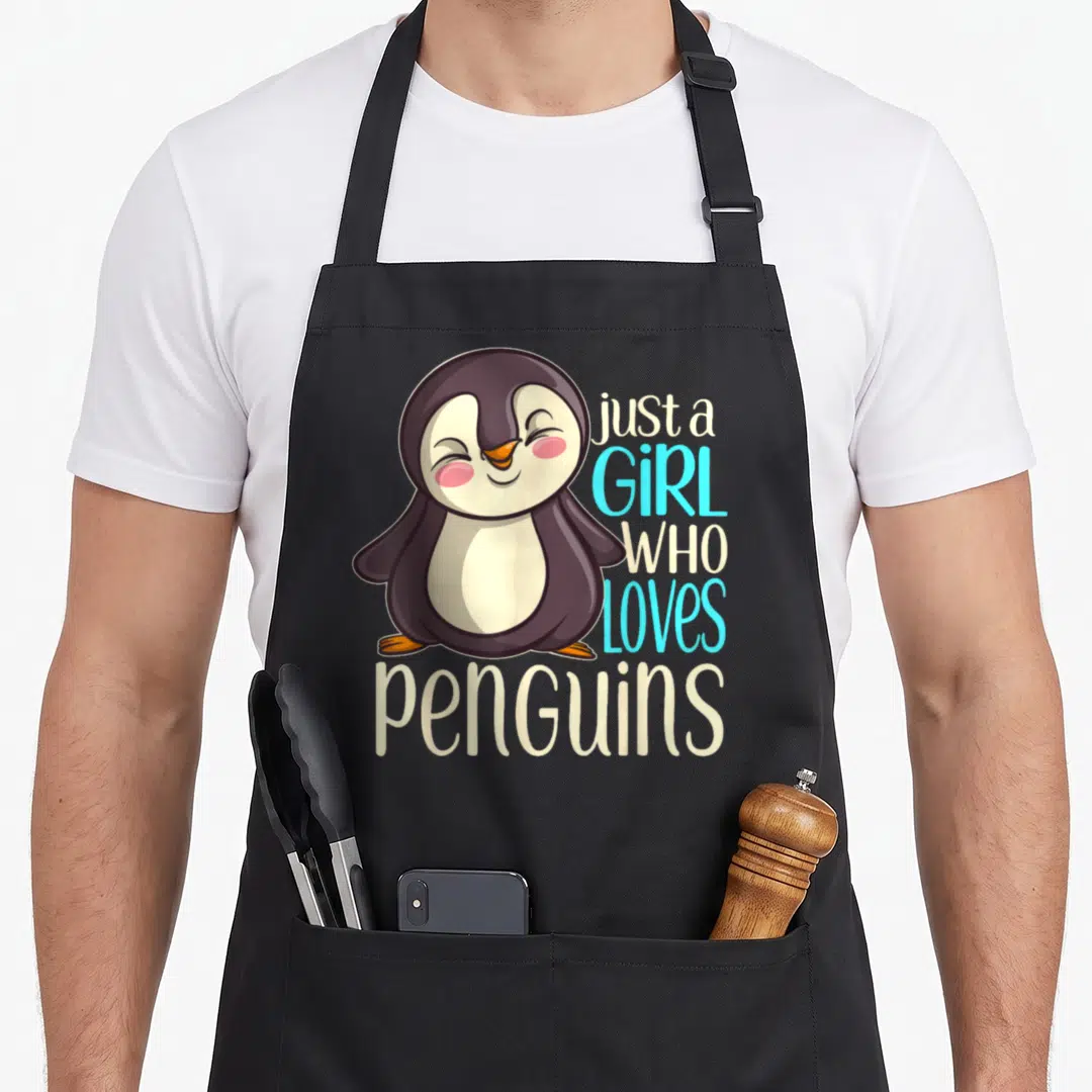 Vintage animal penguin aprons - Cartoon penguin with text just a GIRL WHO loves penguins in purple beige blue white — shown on a black cotton canvas apron against a white background