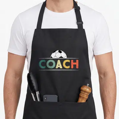 Ball soccer coach apron - Retro distressed soccer ball above multi-colored COACH text sandwiched between white lines — shown on a black cotton canvas apron against a white background