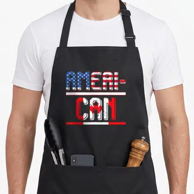 Canadian pride american flag apron - Stacked AMERI-CAN text with US and Canadian flag fills in distressed red white blue — shown on a black cotton canvas apron against a white background