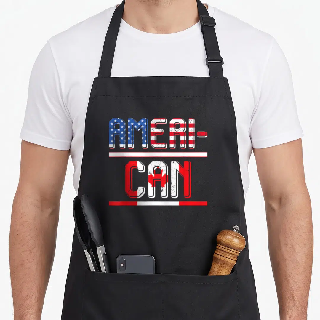 Canadian pride american flag apron - Stacked AMERI-CAN text with US and Canadian flag fills in distressed red white blue — shown on a black cotton canvas apron against a white background