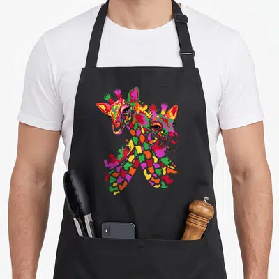 Watercolor giraffe apron - Two cartoon giraffe heads overlapping, filled with pink, orange, green, red, and yellow — shown on a black cotton canvas apron against a white background