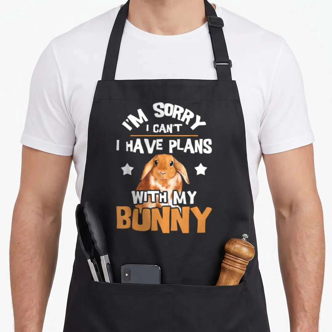 Sorry rabbit apron - Watercolor bunny with I'm sorry I can't I have plans with my bunny text and stars — shown on a black cotton canvas apron against a white background