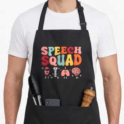 Squad pathologist apron - Four cartoon speech organs below stacked colorful text reading SPEECH SQUAD — shown on a black cotton canvas apron against a white background