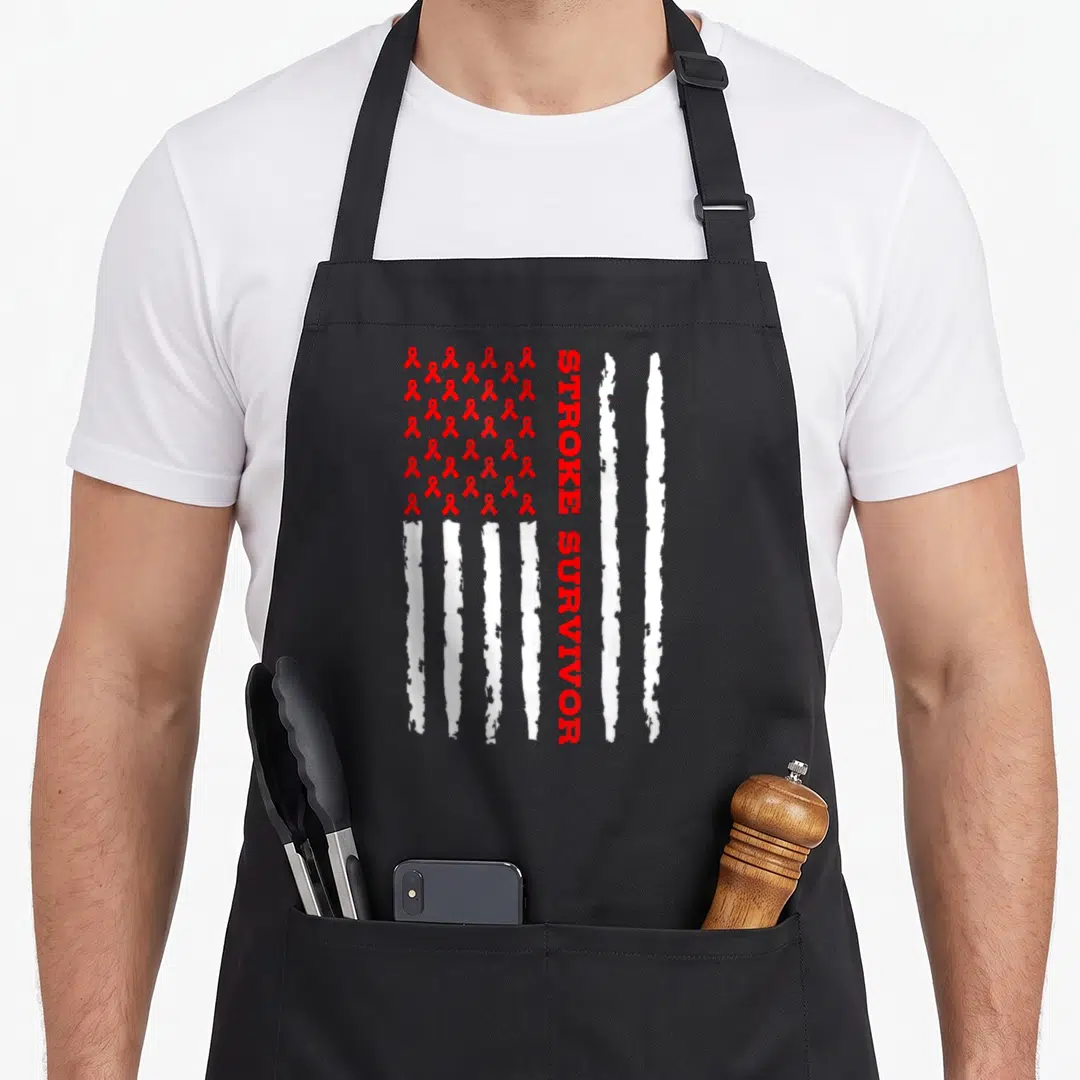 Stroke awareness ribbon apron - Red ribbons and white distressed stripes forming a flag with vertical STROKE SURVIVOR — shown on a black cotton canvas apron against a white background