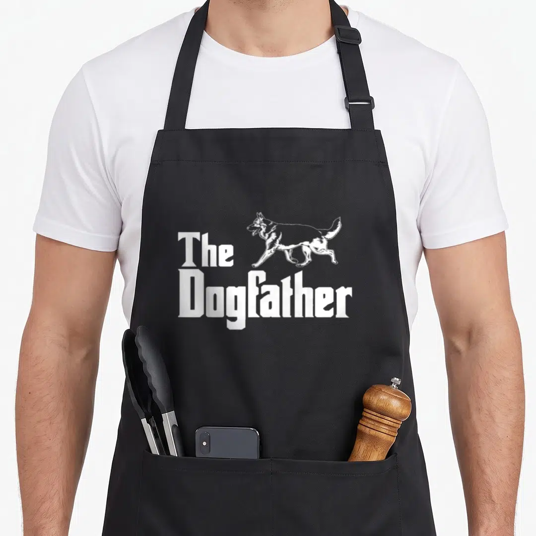 Dogfather shepherd german apron - White line-art German Shepherd walking above bold 'The Dogfather' text — shown on a black cotton canvas apron against a white background