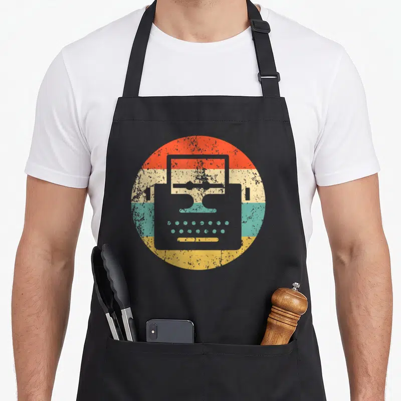 Typewriter writer apron - Grey typewriter silhouette over orange, cream, teal, and yellow horizontal stripes — shown on a black cotton canvas apron against a white background