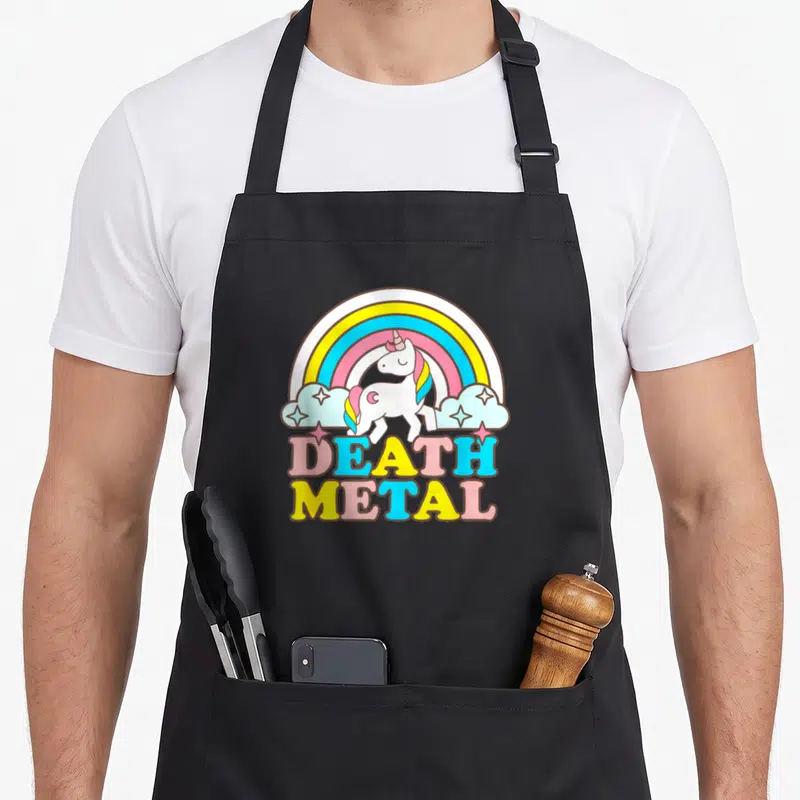 Metal rainbow apron - Cartoon unicorn under rainbow with multi-colored DEATH METAL text — shown on a black cotton canvas apron against a white background