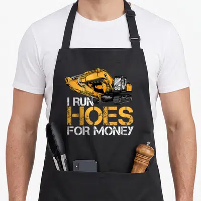 Excavator joke apron - Orange excavator with I Run Hoes For Money distressed text — shown on a black cotton canvas apron against a white background