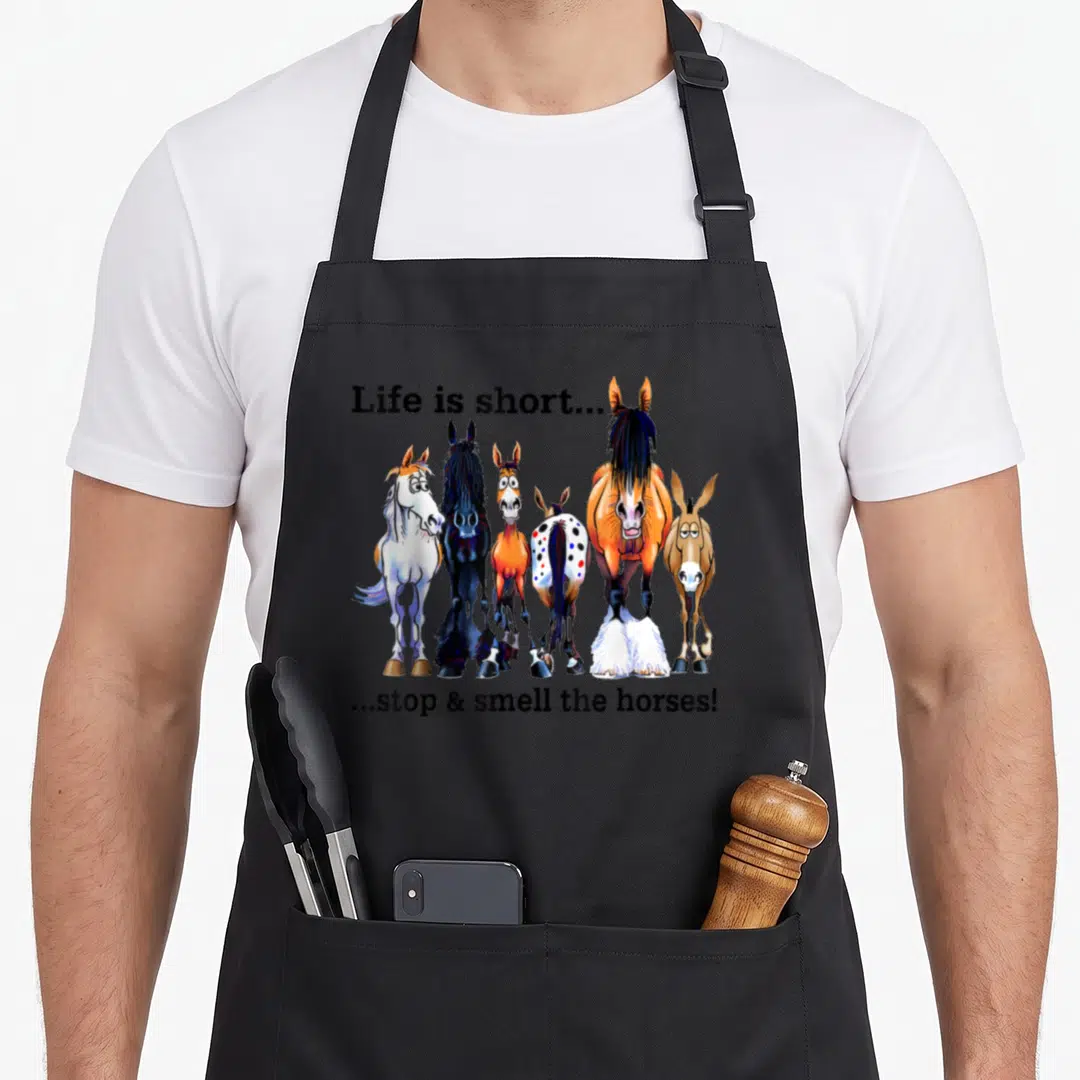 Stop horse apron - Cartoon horses and donkey in orange and brown with split text reading Life is short stop smell horses — shown on a black cotton canvas apron against a white background
