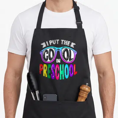 1st pre preschool apron - I PUT THE COOL IN PRESCHOOL text with rainbow gradient sunglasses cartoon art — shown on a black cotton canvas apron against a white background