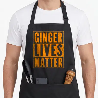 Ginger old lives matter apron - Orange distressed text reading GINGER LIVES MATTER stacked in a rectangle — shown on a black cotton canvas apron against a white background
