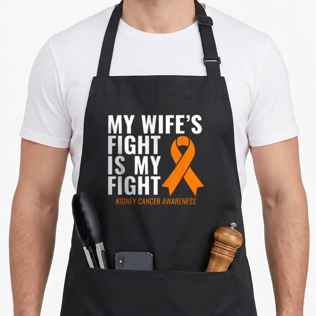 Kidney wife apron - Stacked white text reading My Wife's Fight Is My Fight beside an orange awareness ribbon — shown on a black cotton canvas apron against a white background