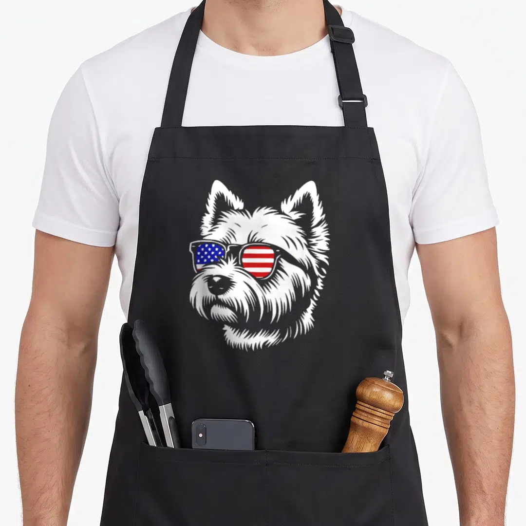 Flag westie apron - Cartoon white dog head wearing sunglasses with red white and blue flag lenses — shown on a black cotton canvas apron against a white background