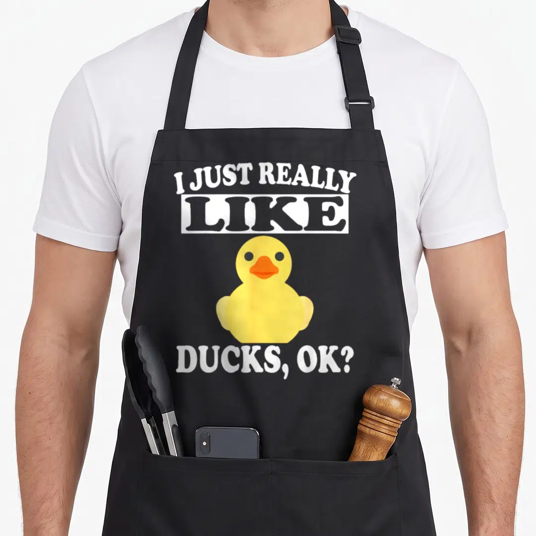 Funny duck apron - Yellow cartoon duck between arched text I JUST REALLY and bottom text DUCKS OK on white box — shown on a black cotton canvas apron against a white background