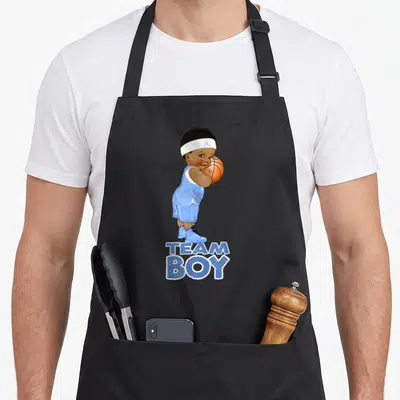 Ethnic basketball boys apron - Cartoon baby in blue kit holding orange ball above text TEAM BOY — shown on a black cotton canvas apron against a white background