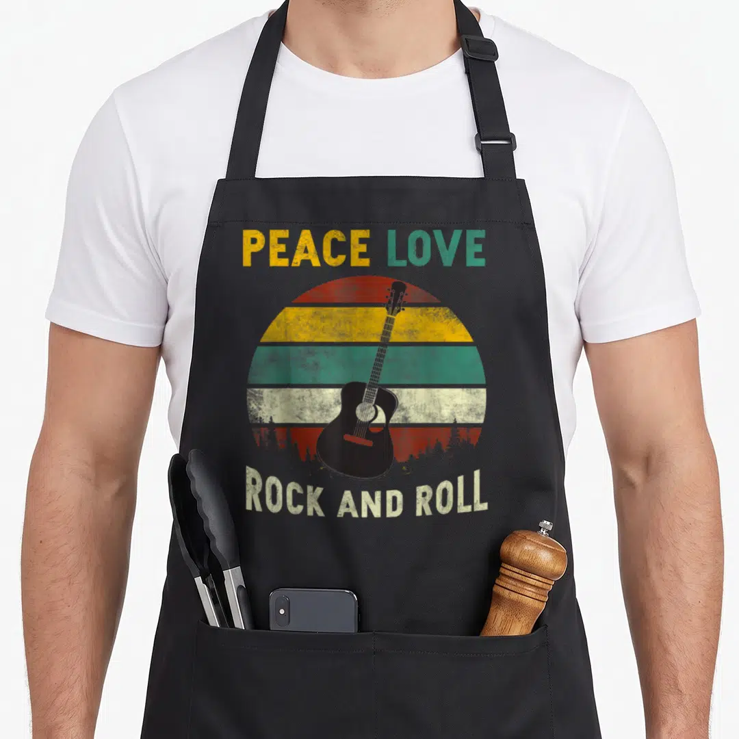 Rock peace apron - Black guitar over retro red yellow green striped sun with forest silhouette and PEACE LOVE ROCK — shown on a black cotton canvas apron against a white background