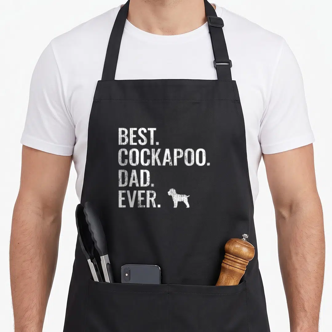 Dog owner cockapoo apron - White distressed text reading best cockapoo dad ever with small dog silhouette on left — shown on a black cotton canvas apron against a white background