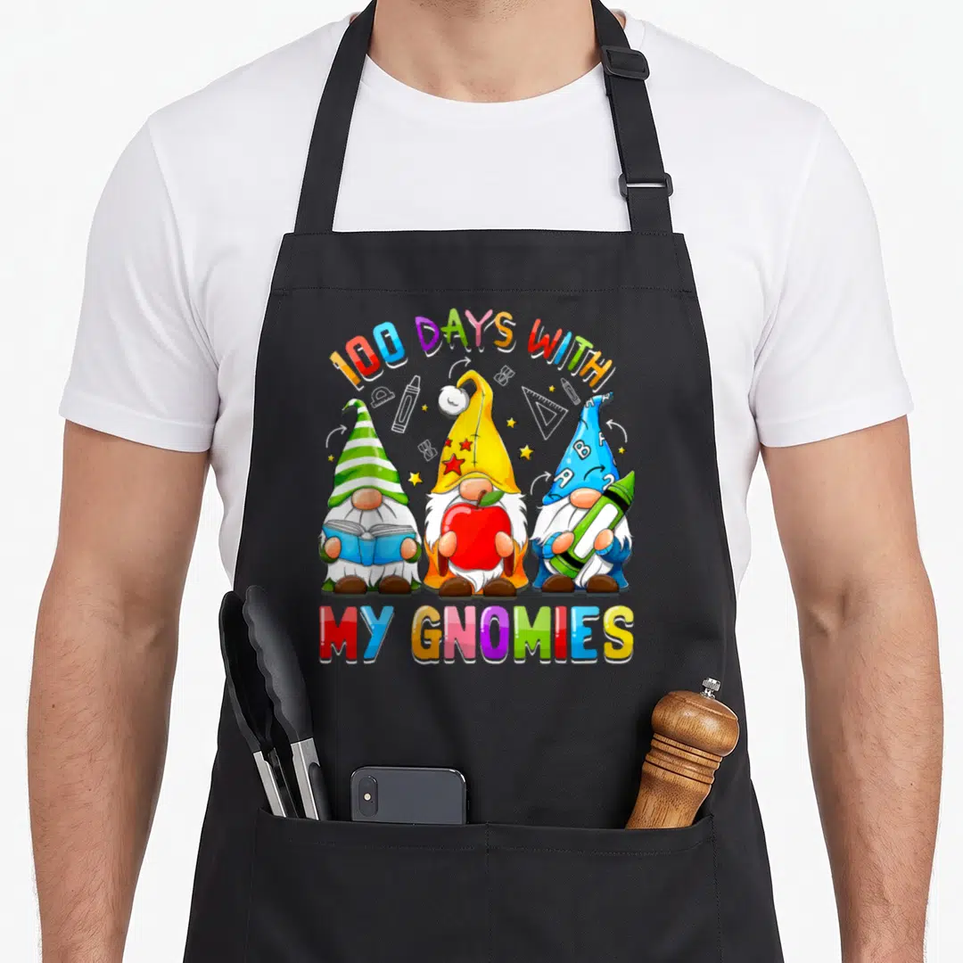 Gnome teacher apron - Three cartoon gnomes with school supplies under arching text 100 DAYS WITH MY GNOMIES — shown on a black cotton canvas apron against a white background