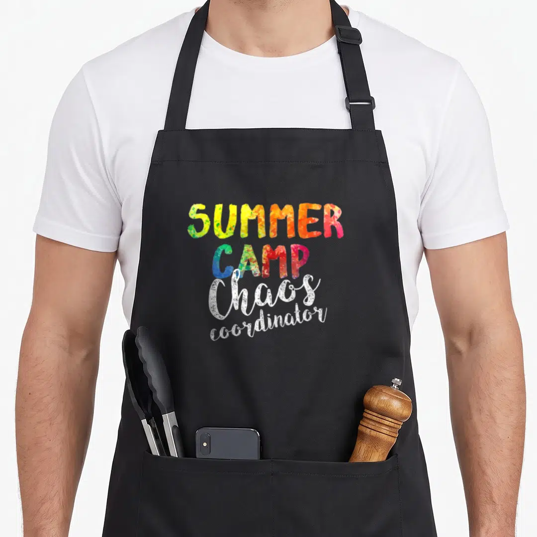 Chao camp chef apron - Stacked text reading SUMMER CAMP Chaos coordinator in colorful speckled and white fonts — shown on a black cotton canvas apron against a white background
