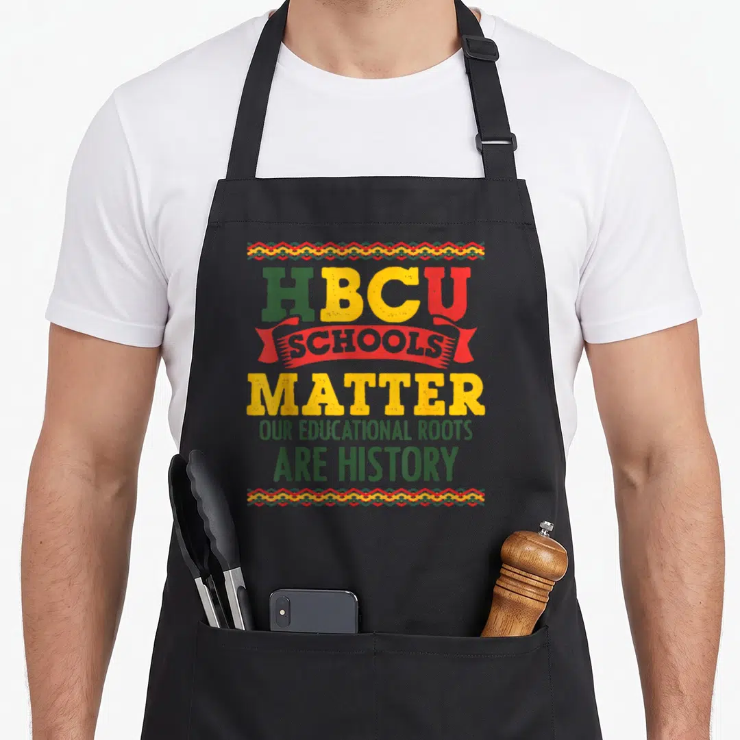 College african american aprons - HBCU SCHOOLS MATTER text on red ribbon with green yellow red zigzag borders — shown on a black cotton canvas apron against a white background