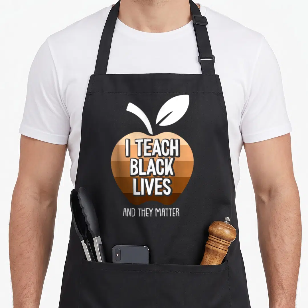 Teach blm camping apron - Brown striped apple with white text reading I TEACH BLACK LIVES AND THEY MATTER — shown on a black cotton canvas apron against a white background