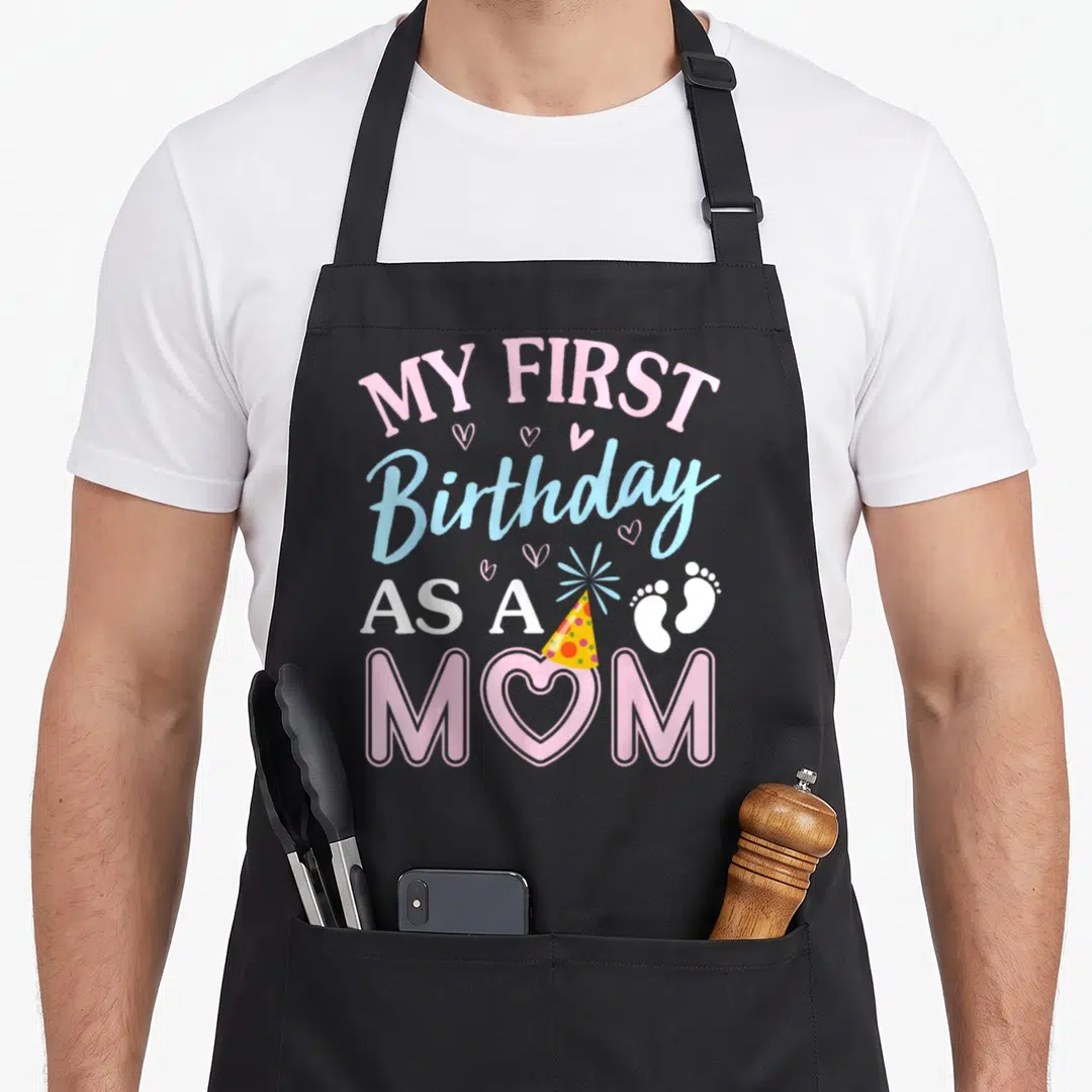 Birthday mama mother's day aprons - My First Birthday As A Mom text with heart, party hat, and footprints in pink — shown on a black cotton canvas apron against a white background