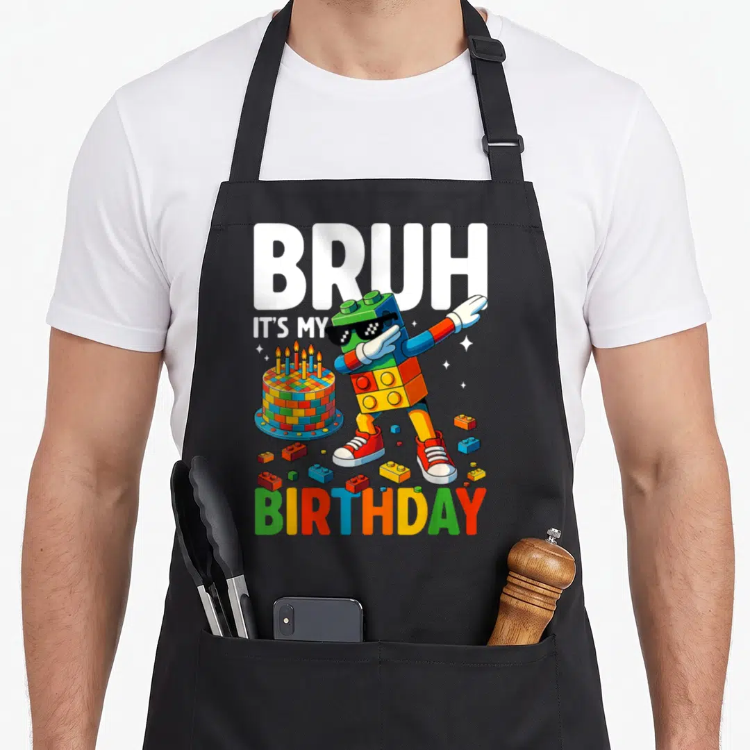 Dabbing block & apron - Brick figure dabbing with cake and BRUH IT'S MY BIRTHDAY text in primary colors — shown on a black cotton canvas apron against a white background
