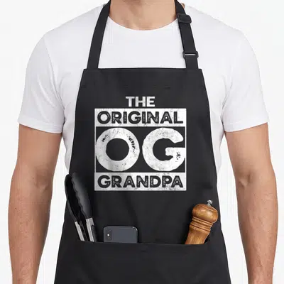 Original grandad aprons - White stacked text reading THE ORIGINAL OG GRANDPA inside a rectangular frame — shown on a black cotton canvas apron against a white background