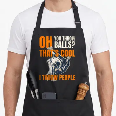 Jujutsu judo apron - Distressed orange and blue text with upside-down judo thrower graphic — shown on a black cotton canvas apron against a white background