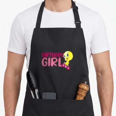 Tweety floral aprons - Pink BIRTHDAY GIRL text next to yellow bird holding pink flowers — shown on a black cotton canvas apron against a white background