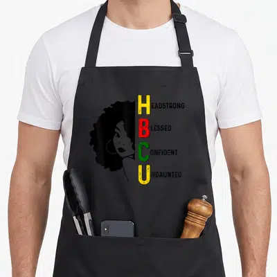 Abbreviation historical aprons - Black woman profile beside vertical HBCU letters in yellow red green spelling — shown on a black cotton canvas apron against a white background