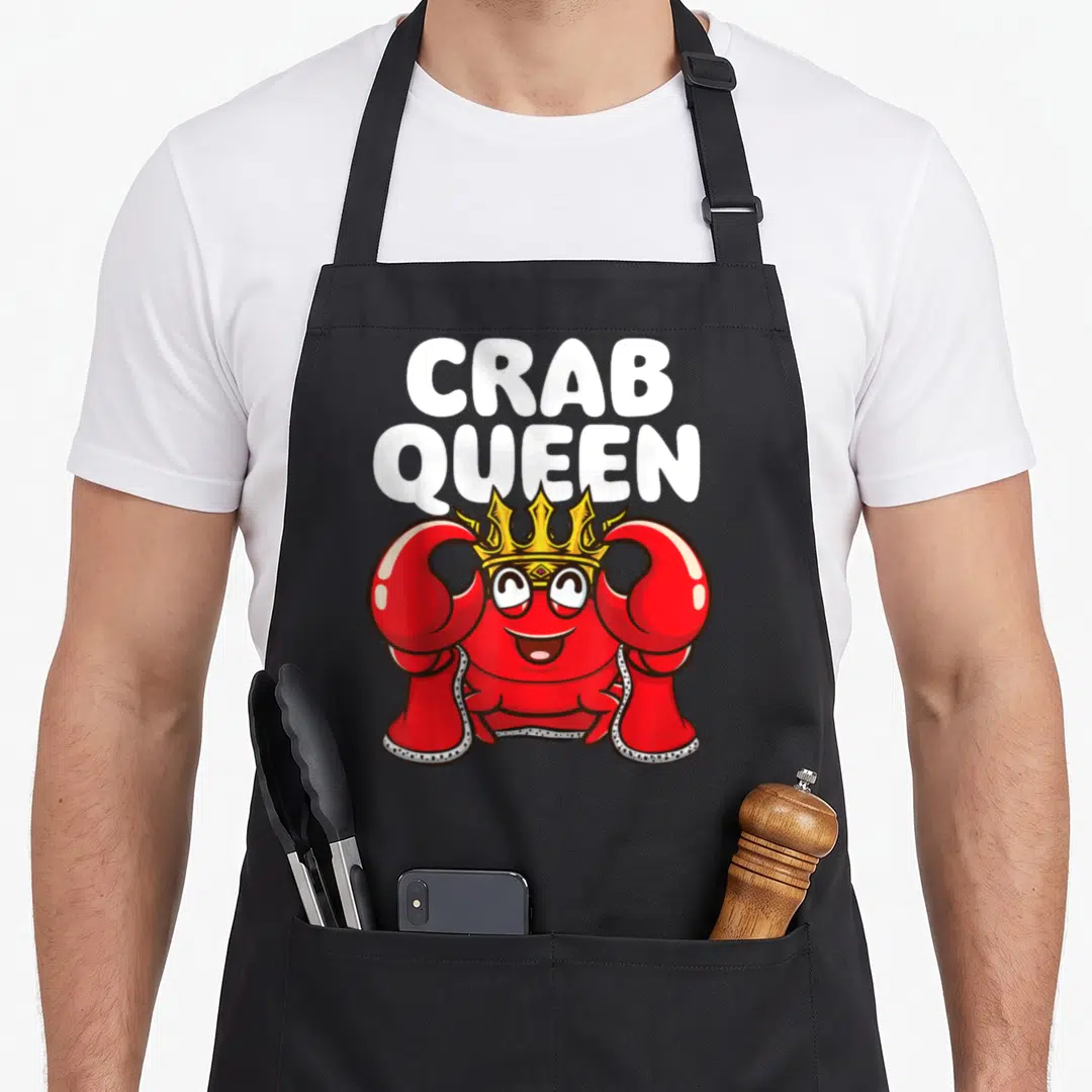Hunting crab apron - Cartoon red crab wearing yellow crown and cape under white stacked CRAB QUEEN text — shown on a black cotton canvas apron against a white background