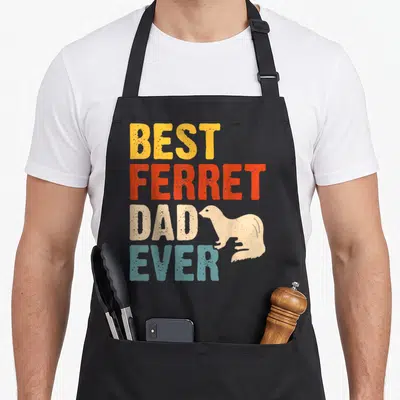 Ferret dad apron for dad - Stacked BEST FERRET DAD EVER text with beige ferret silhouette in yellow red beige — shown on a black cotton canvas apron against a white background