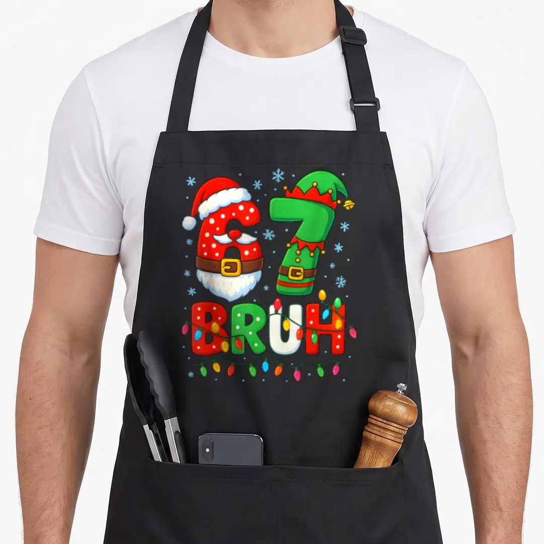 Six christmas elf apron - Number 67 dressed as Santa and Elf with BRUH text wrapped in Christmas lights — shown on a black cotton canvas apron against a white background