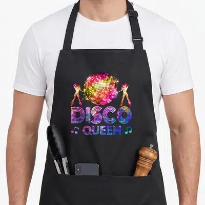 Disco queen 70s apron - Multi-colored disco ball with two dancers and stacked DISCO QUEEN text — shown on a black cotton canvas apron against a white background