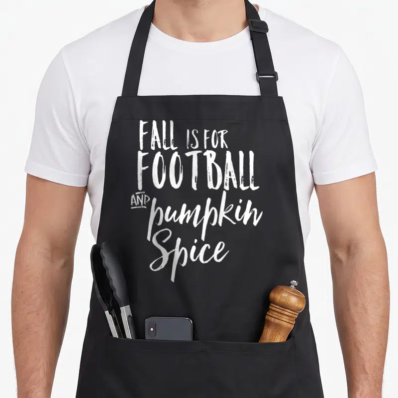 Football spice apron - White stacked typography reading FALL IS FOR FOOTBALL AND pumpkin Spice — shown on a black cotton canvas apron against a white background