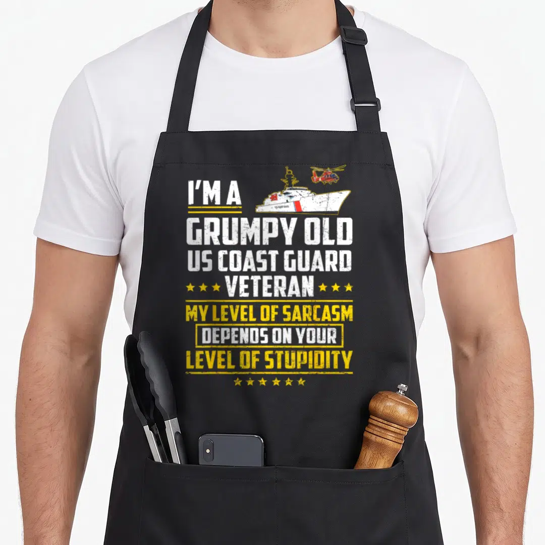 Grumpy us aprons - Distressed text I'm a grumpy old US Coast Guard veteran with ship and helicopter illustration — shown on a black cotton canvas apron against a white background