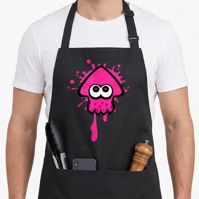 Inkling squid apron - Pink cartoon inkling head with large eyes on a pink ink splatter with a downward drip and black — shown on a black cotton canvas apron against a white background
