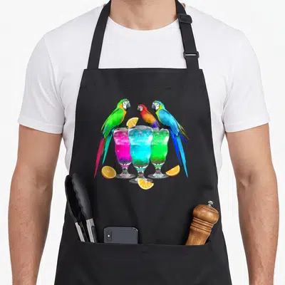 Drinking hawaiian apron - Three colorful parrots perched on pink, blue, and green cocktails with orange slices — shown on a black cotton canvas apron against a white background
