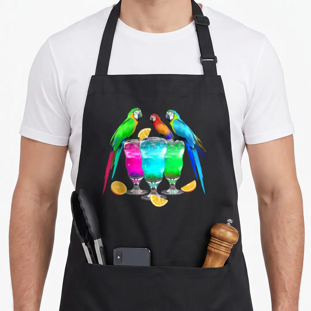 Drinking hawaiian apron - Three colorful parrots perched on pink, blue, and green cocktails with orange slices — shown on a black cotton canvas apron against a white background