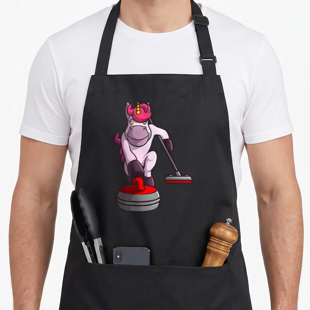 Curling unicorn apron - Cartoon white and pink unicorn pushing a red and grey curling stone while holding a broom — shown on a black cotton canvas apron against a white background