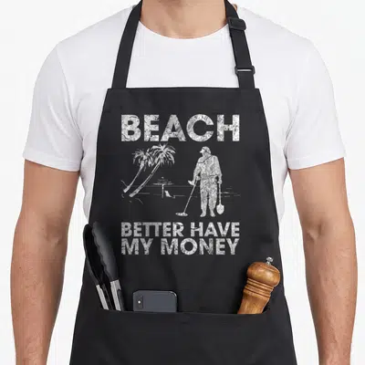 Better money apron - Grey background with white foil-textured text reading Beach Better Have My Money above a golfer — shown on a black cotton canvas apron against a white background
