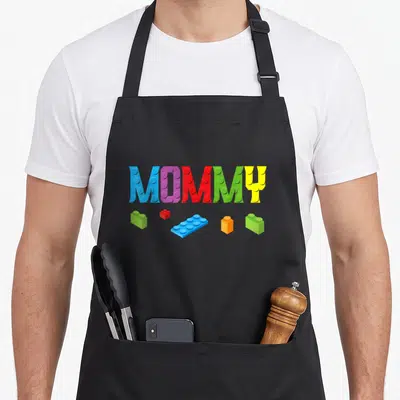 Brick family block & apron - MOMMY text in blue purple red green yellow toy bricks with five scattered blocks below — shown on a black cotton canvas apron against a white background