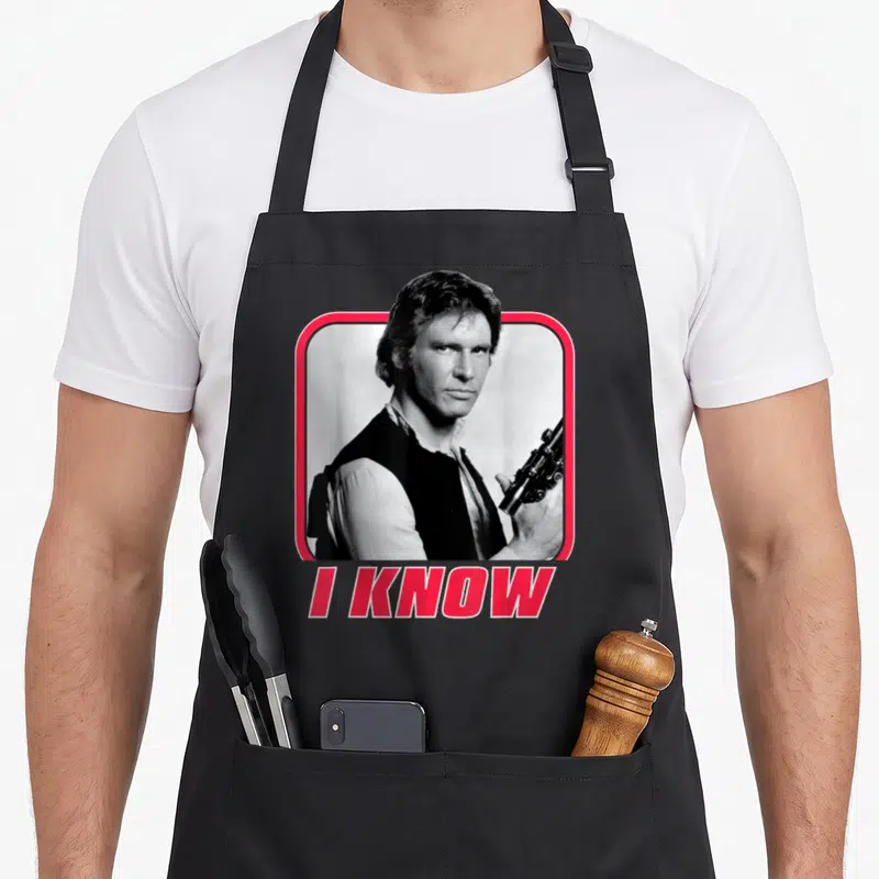 Holiday valentine's day apron - Man holding gun in red frame with I KNOW text below — shown on a black cotton canvas apron against a white background