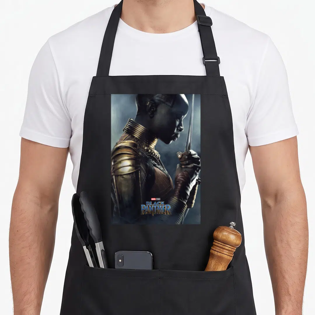 Okoye general apron - Profile portrait of woman in gold armor holding spear with Marvel Studios Black Panther text — shown on a black cotton canvas apron against a white background