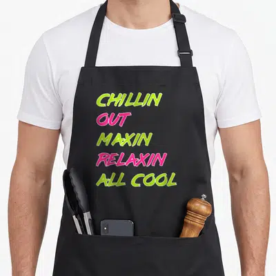 Chillin fresh air apron - Stacked lime green and pink text reading CHILLIN OUT MAXIN RELAXIN ALL COOL — shown on a black cotton canvas apron against a white background