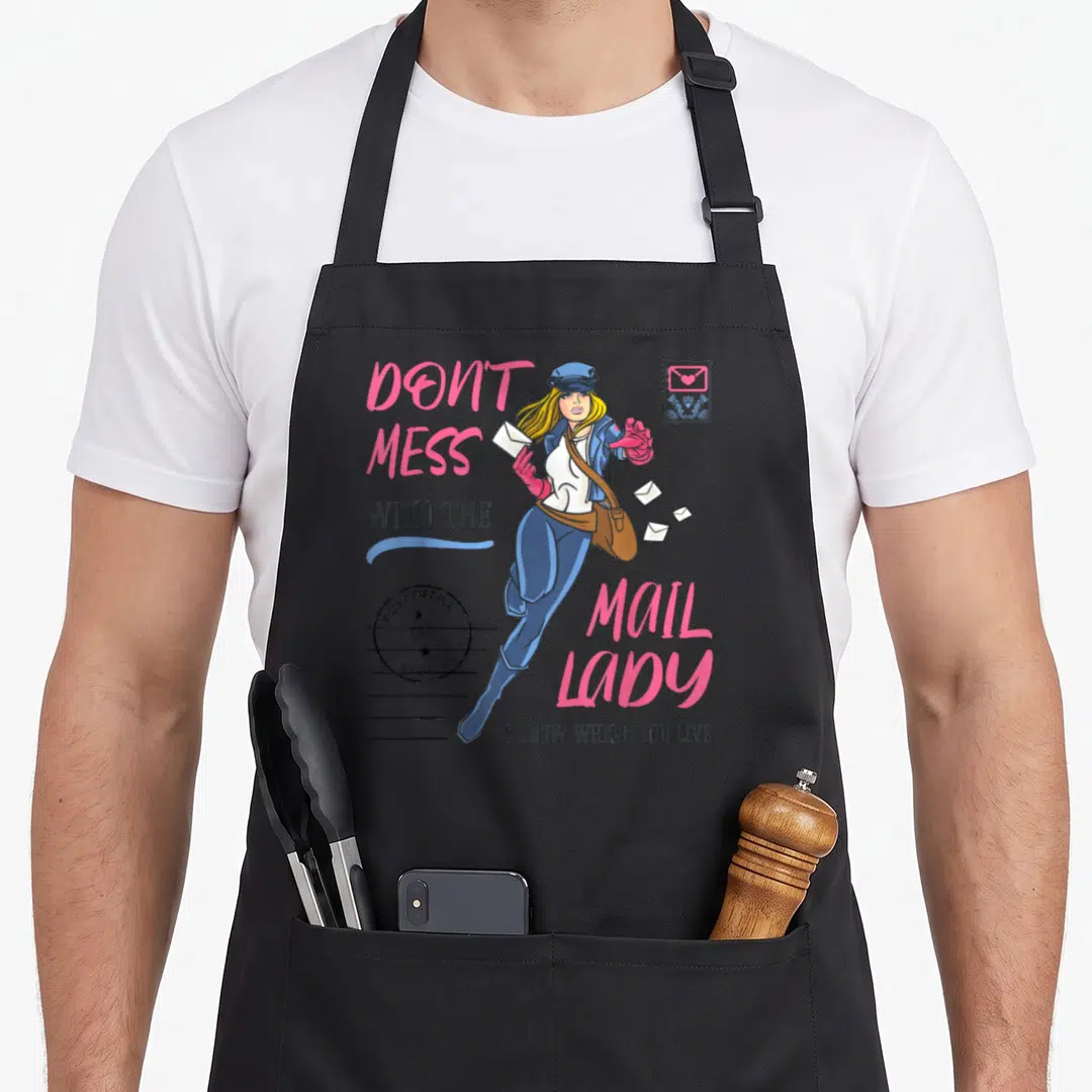 Mess postal aprons - Cartoon mail lady with pink text, stamp, and postmark on grey background — shown on a black cotton canvas apron against a white background